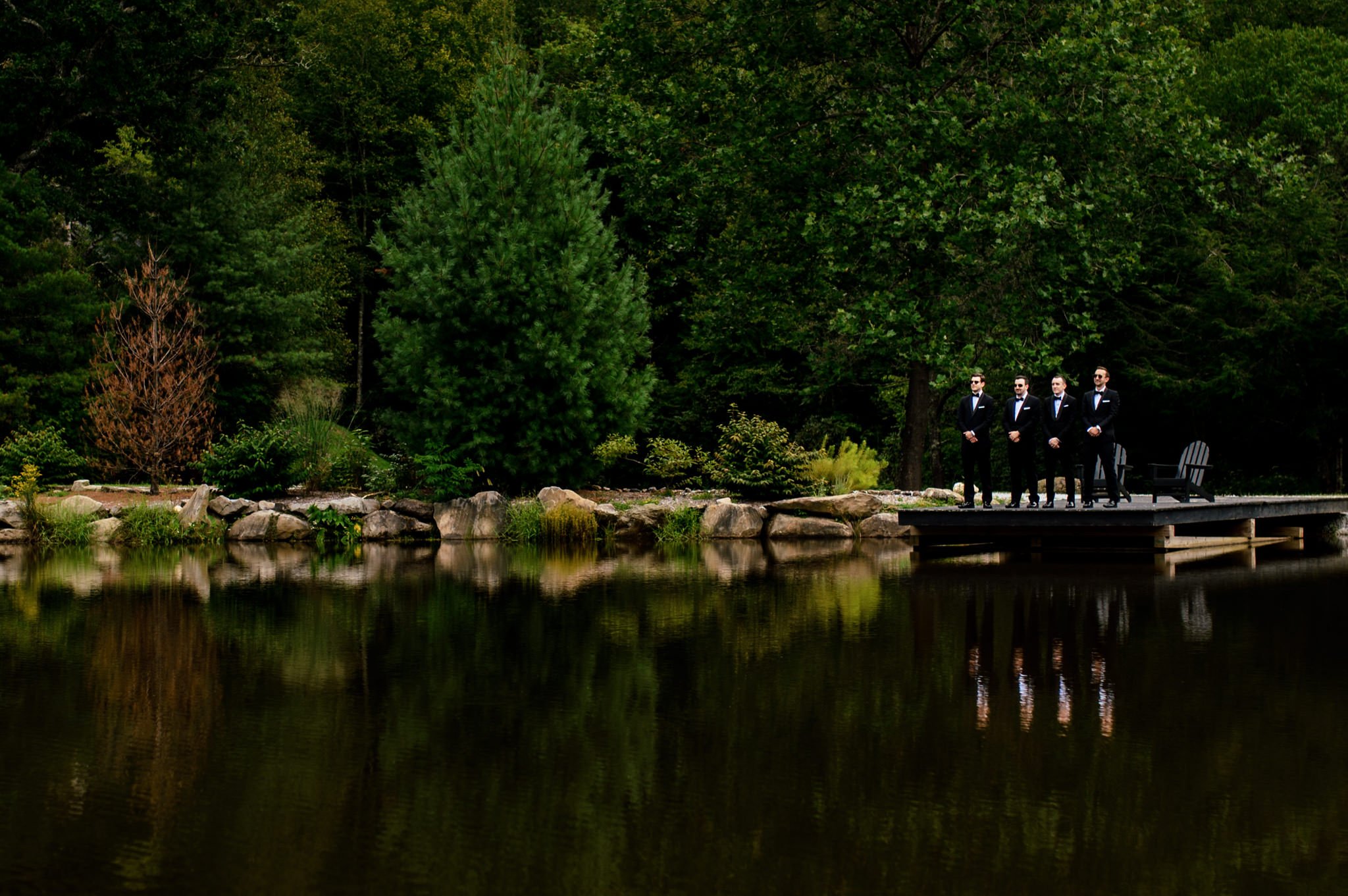 Groomsmen standing on a dock near a pond.