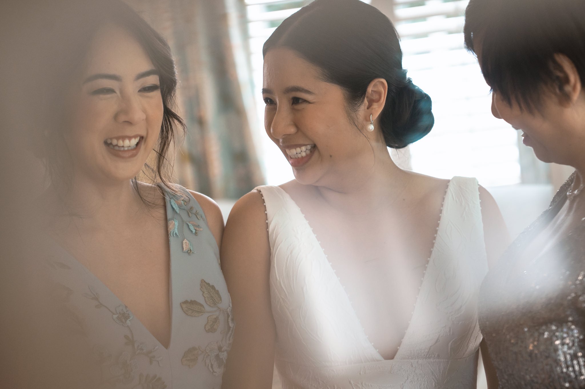 A bride and her bridesmaids are laughing in front of a mirror.