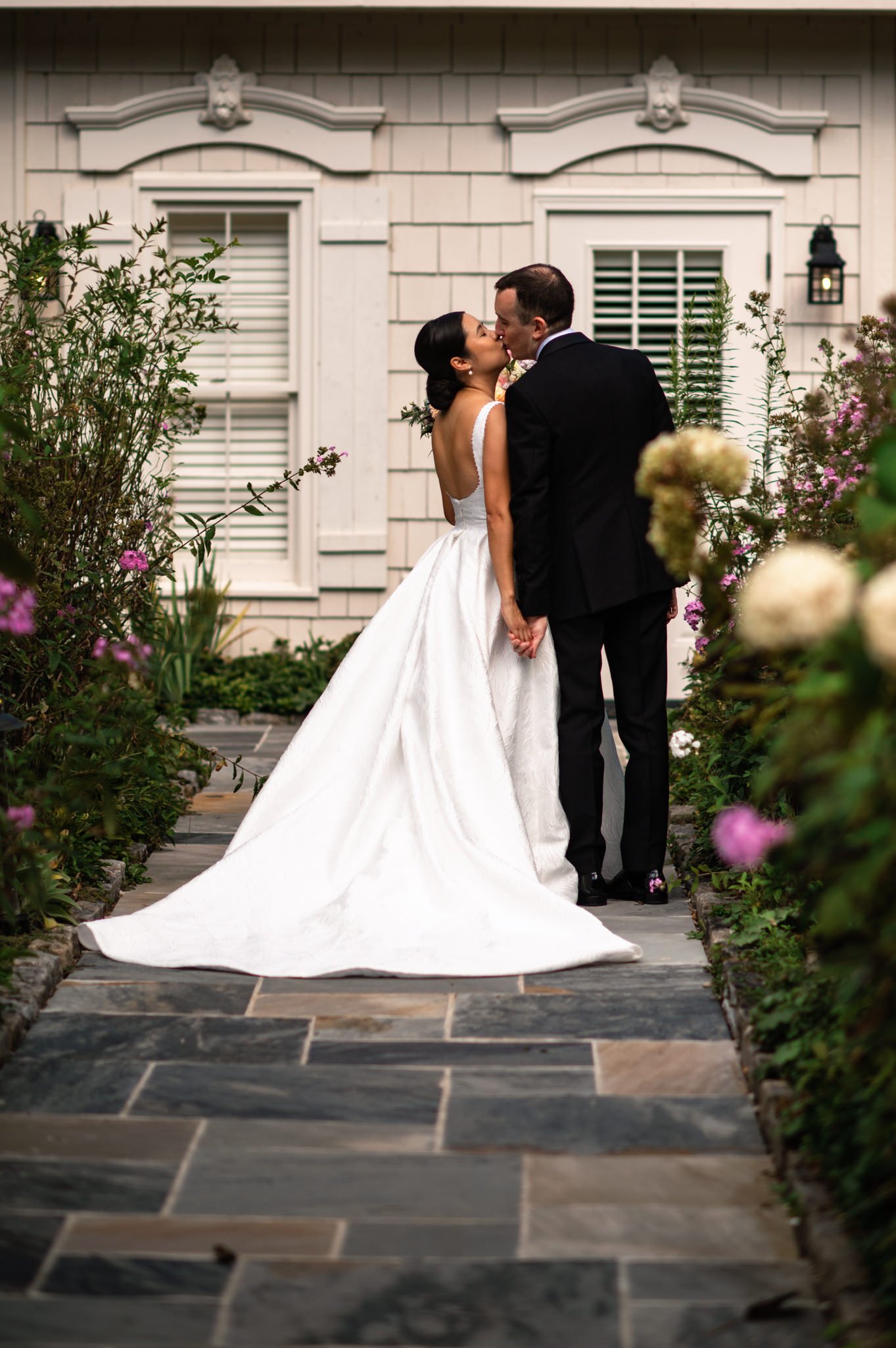 A bride and groom kiss in front of a house.