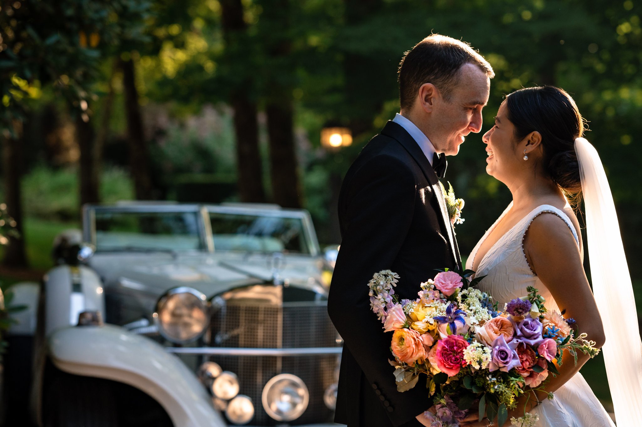 A bride and groom in front of a classic car at their farm wedding.