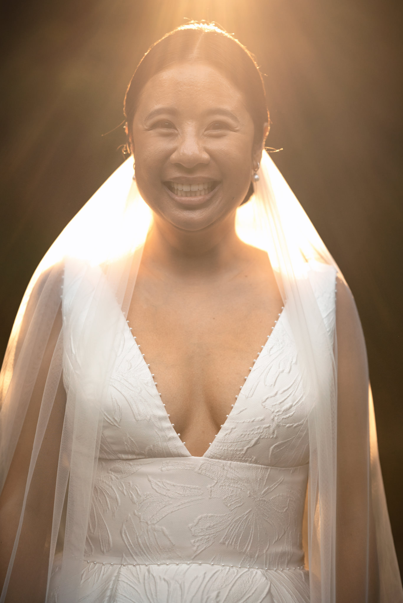 A bride smiles at her farm wedding as the sun shines through her veil.
