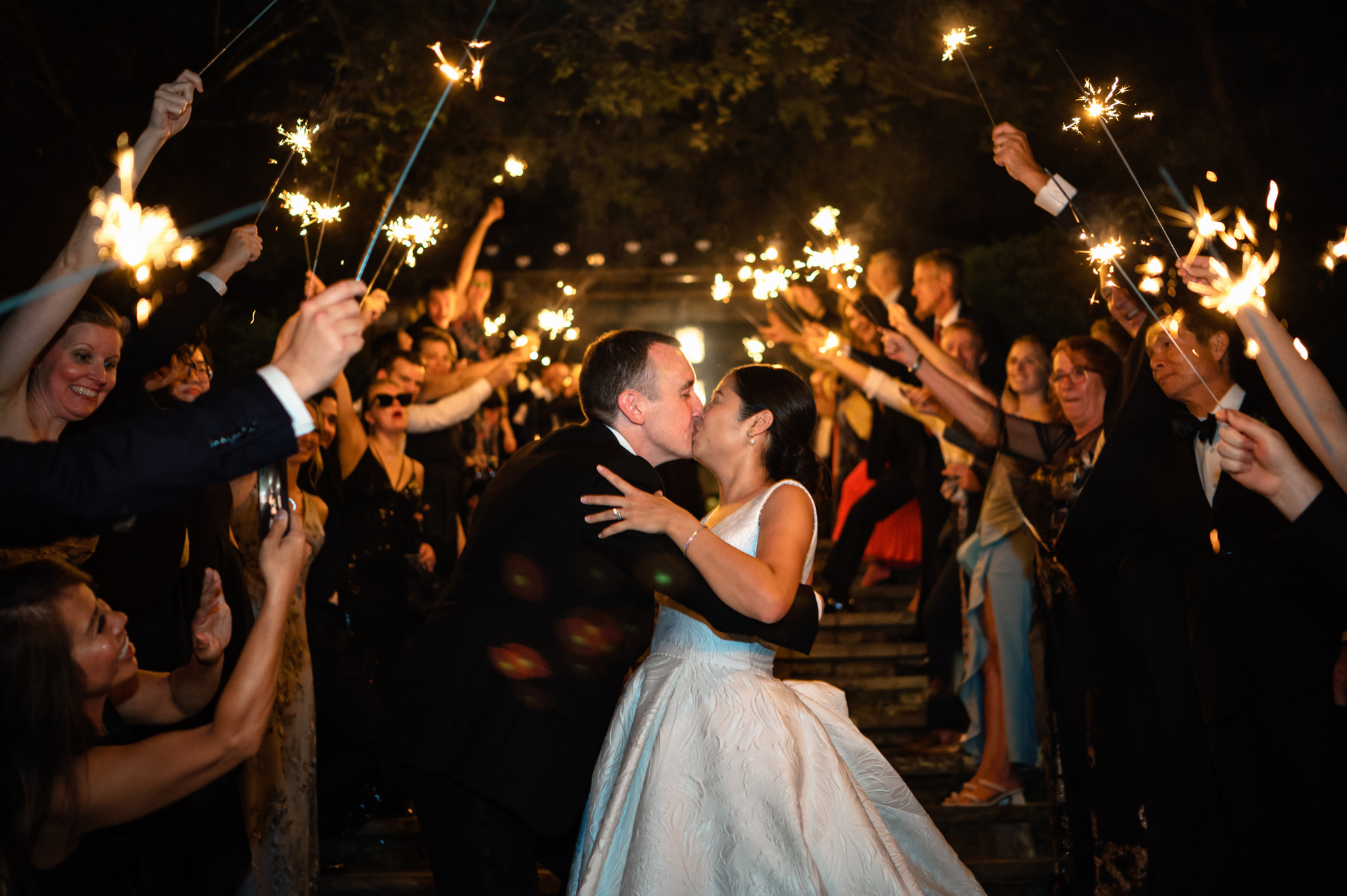 A bride and groom sharing a romantic kiss in front of sparklers at their farm wedding.