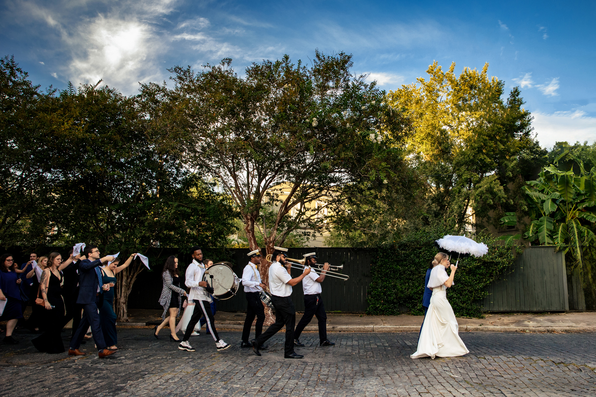 A group of brides and grooms walking down a street with umbrellas in New Orleans.