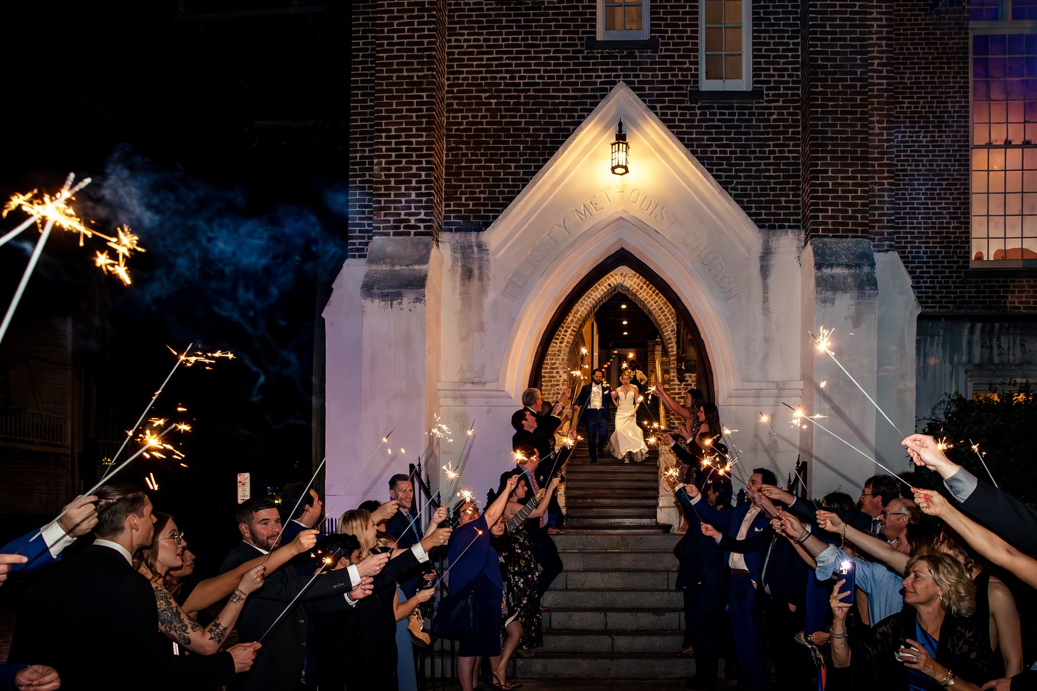 A group of people holding sparklers outside of a church in New Orleans for a joyous wedding celebration.