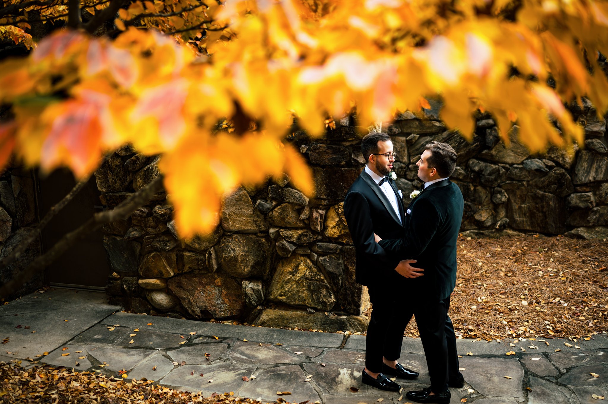 Two men in tuxedos standing in front of autumn leaves at the Seely Pavilion for a Grove Park Inn wedding.