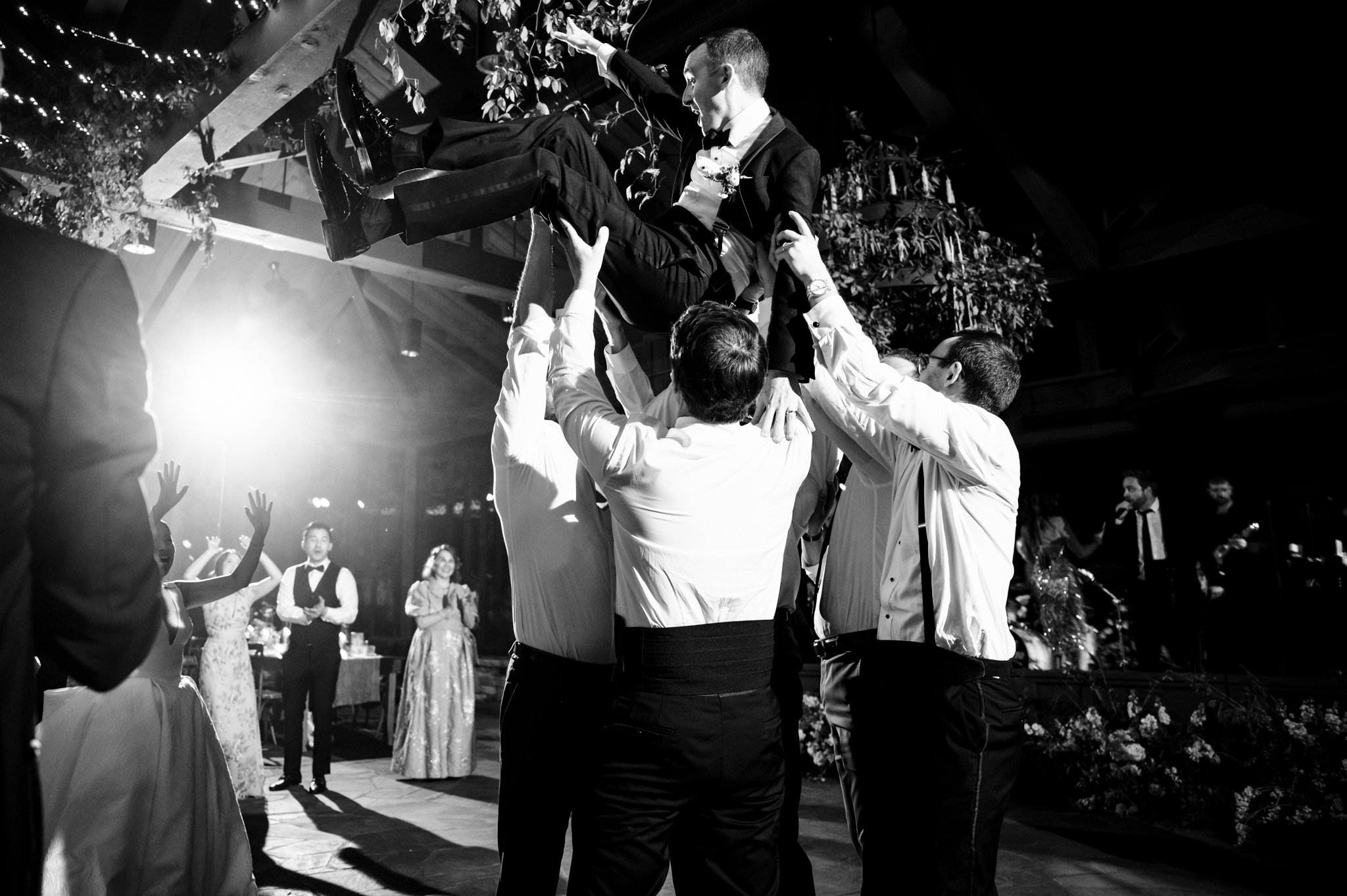 A black and white photo of a group of best men holding up a bride.