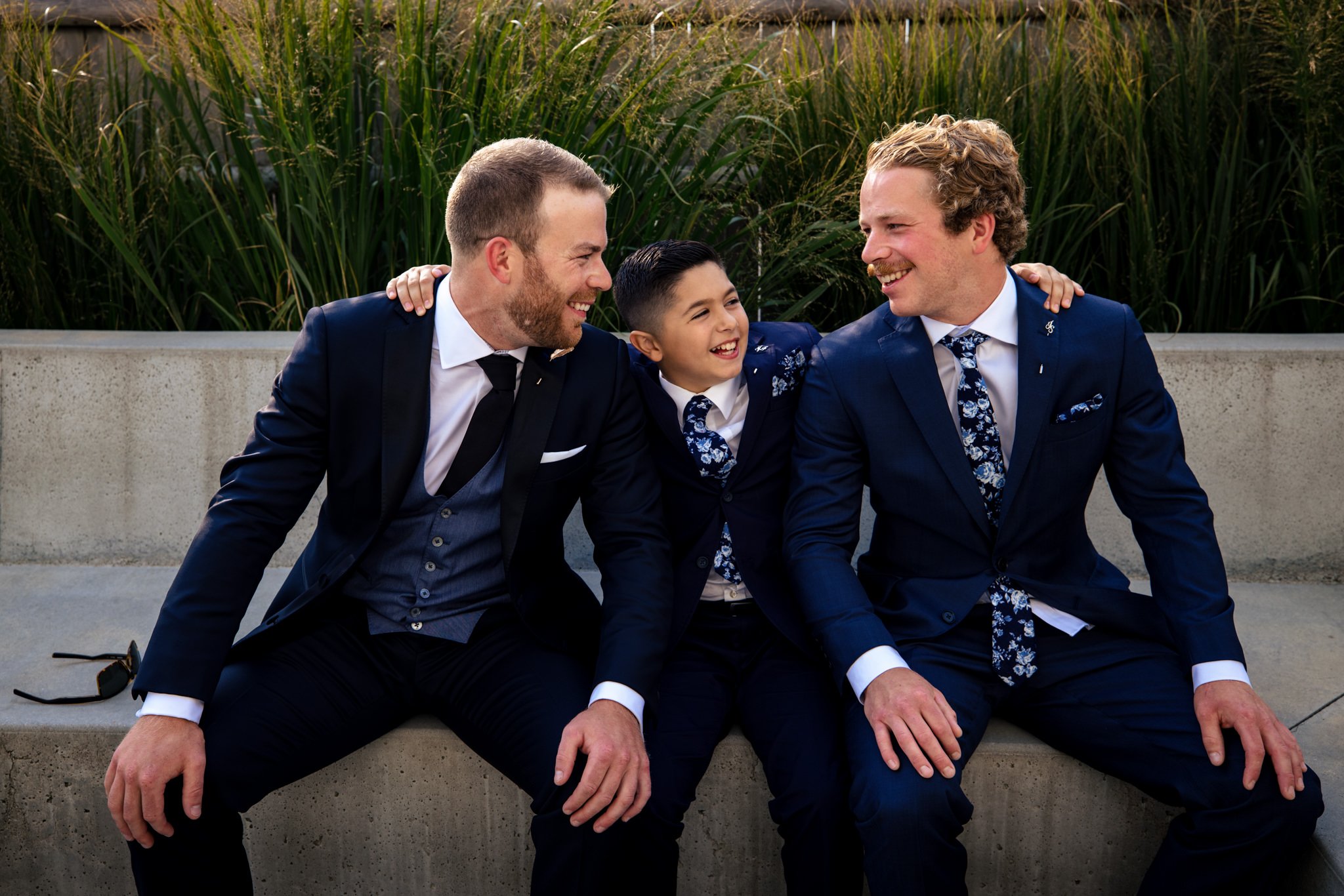 Three best men in suits and ties sitting on a bench.