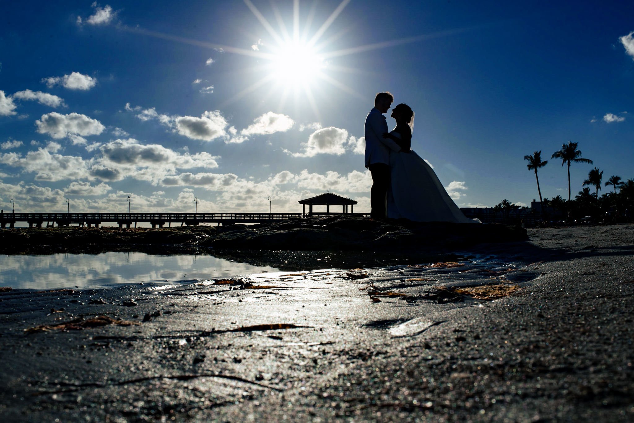 An Asheville, NC wedding photographer captures a beautiful bride and groom standing on a beach with the sun behind them.
