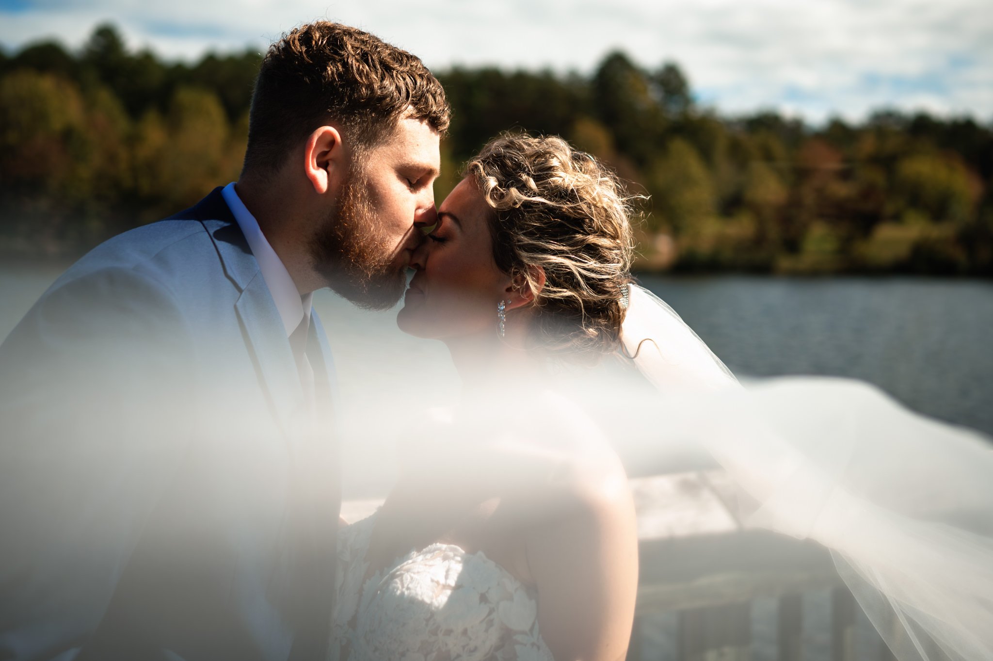 A beautiful moment captured in photography as a bride and groom share a passionate kiss against the serene backdrop of a lake.