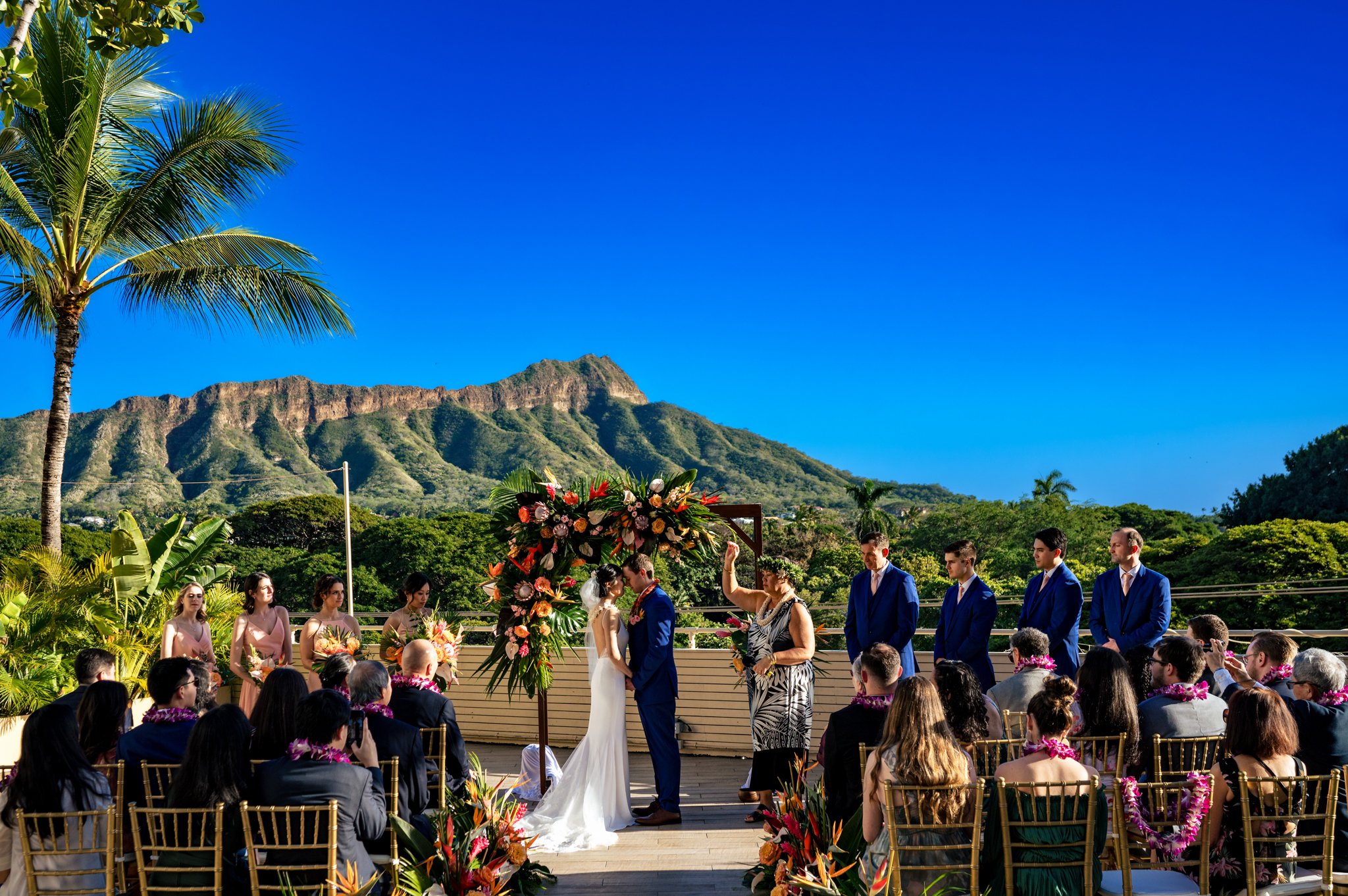 A wedding ceremony in hawaii with palm trees and mountains in the background.