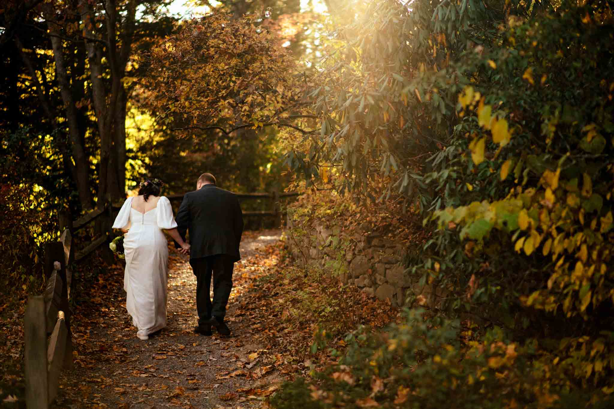 A couple walks down a path in the woods during their Asheville Botanical Gardens wedding, captured beautifully through photography.