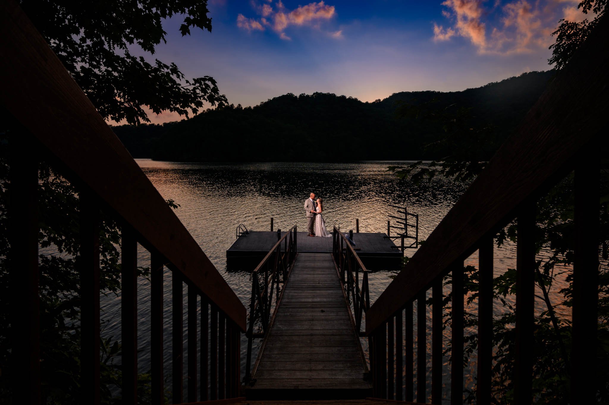 A bride and groom standing on a dock at sunset during their Nantahala wedding.