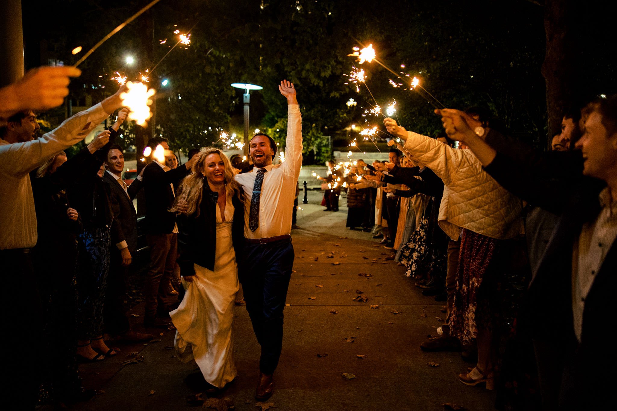 An Asheville wedding couple holding sparklers as they walk down the street.
