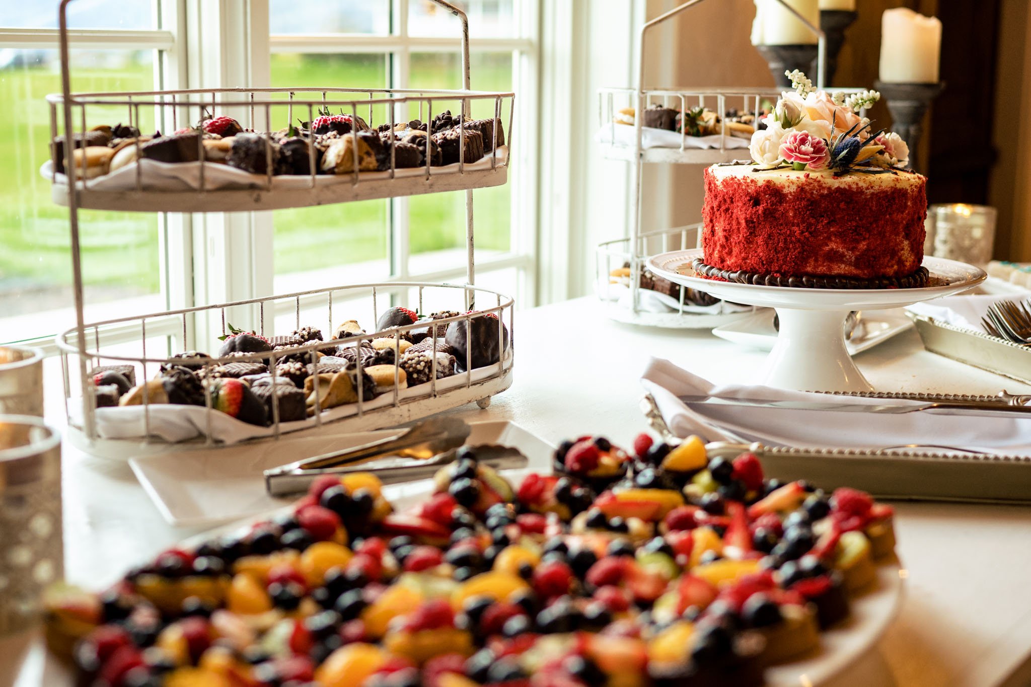 Elegant dessert buffet at an Asheville wedding featuring a red velvet cake on a stand, surrounded by assorted mini desserts, including fruit tarts and chocolate bites, in a room with a view.