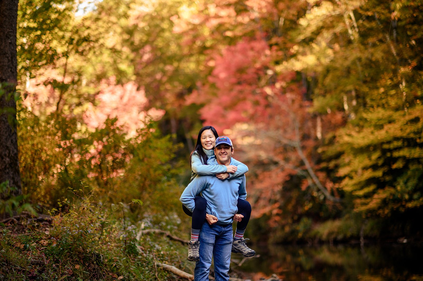 A man giving a piggyback ride to a woman in a forest with colorful autumn foliage near Linville Falls.